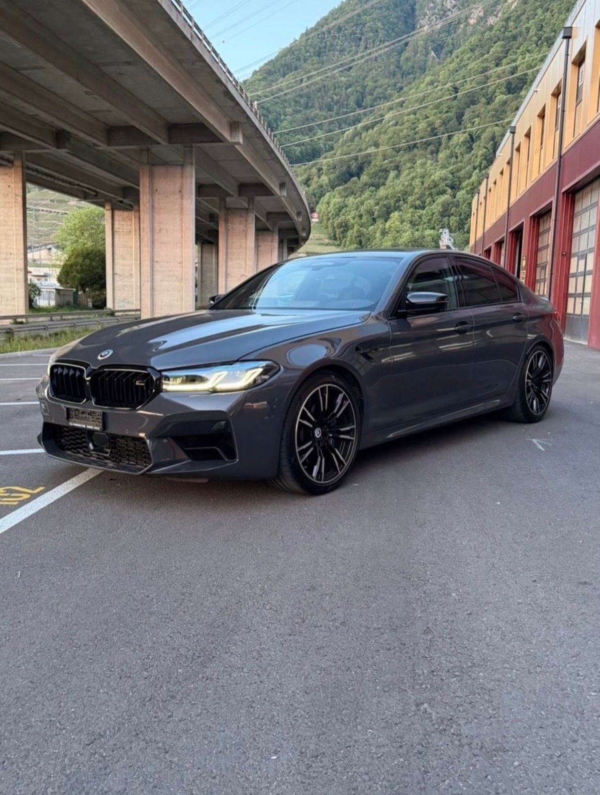 BMW M5 Competition grise, garée sous un viaduc en Valais