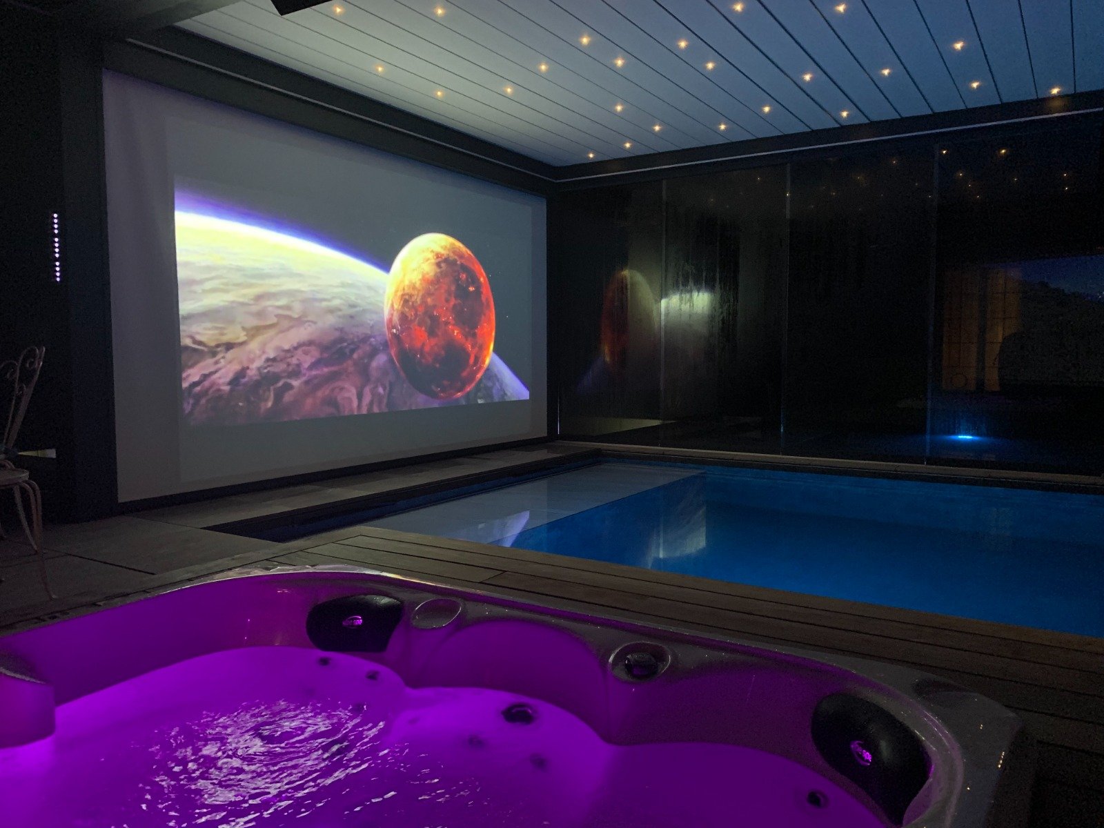 Film projeté sur l'écran géant de Secret Paradise, vu depuis le jacuzzi éclairé en violet au bord de la piscine
