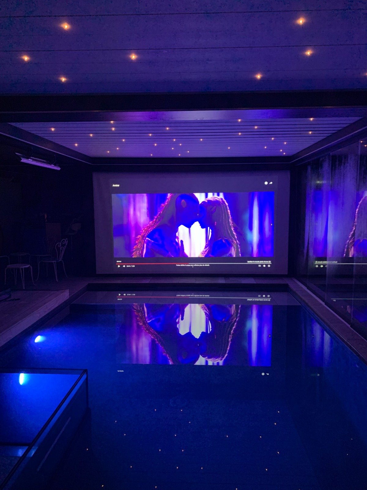 Écran géant allumé la nuit à Secret Paradise, son reflet courant sur toute la longueur de la piscine sous un plafond étoilé