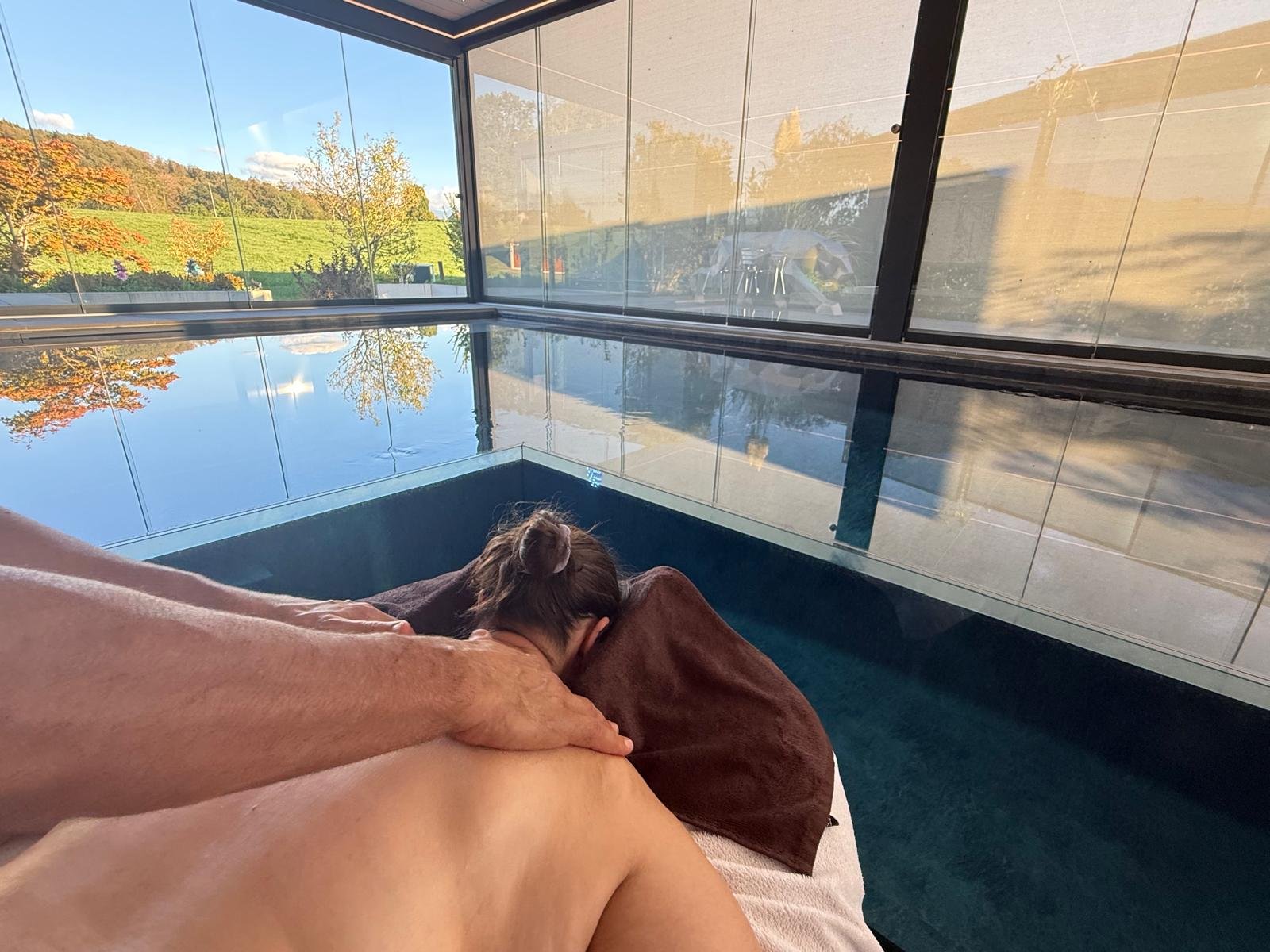 Massage en cours au bord du bassin de Secret Paradise, face aux baies vitrées ouvertes sur la campagne en automne