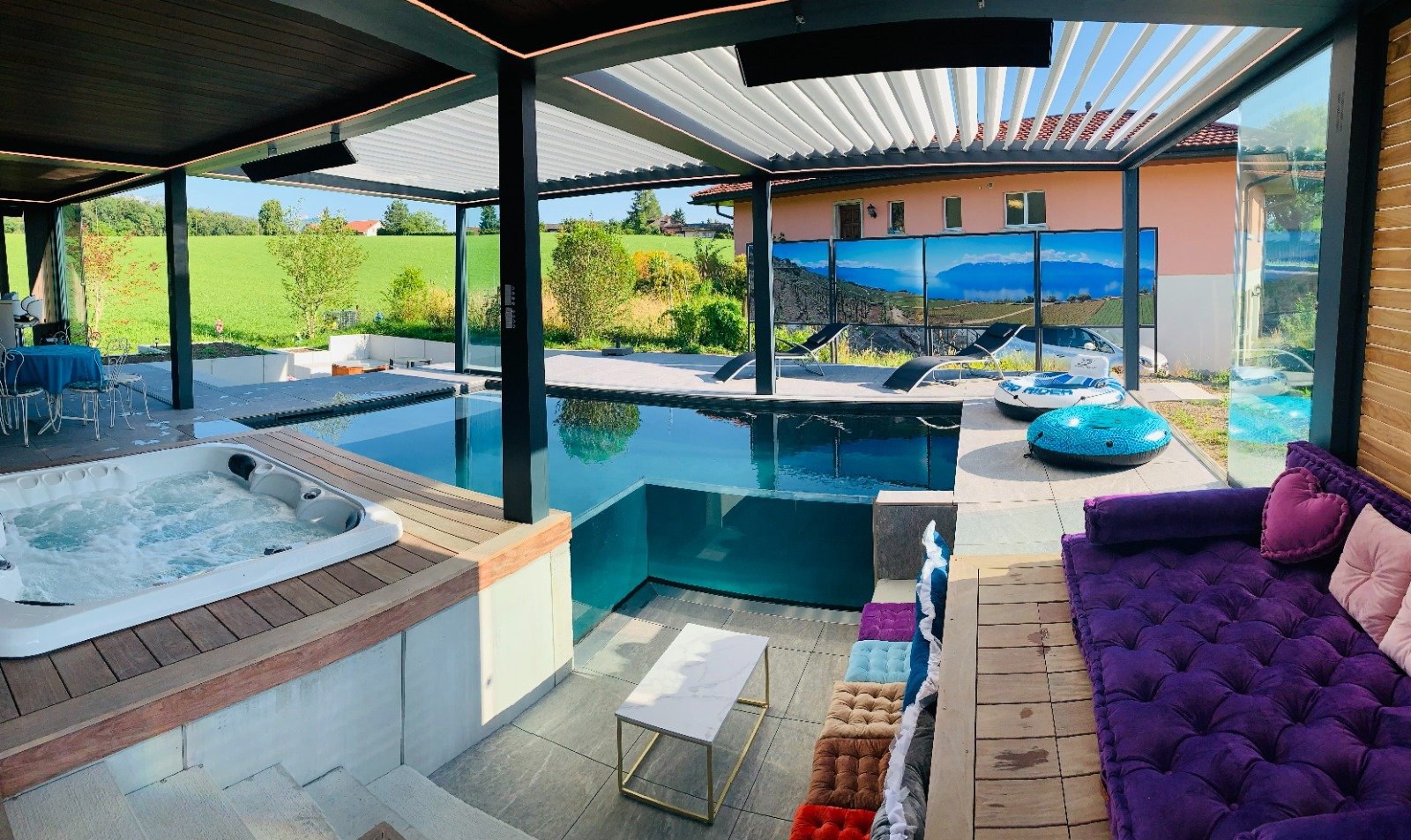 Vue d'ensemble de Secret Paradise en journée : jacuzzi, piscine intérieure, banquette et baies vitrées ouvertes sur la campagne vaudoise