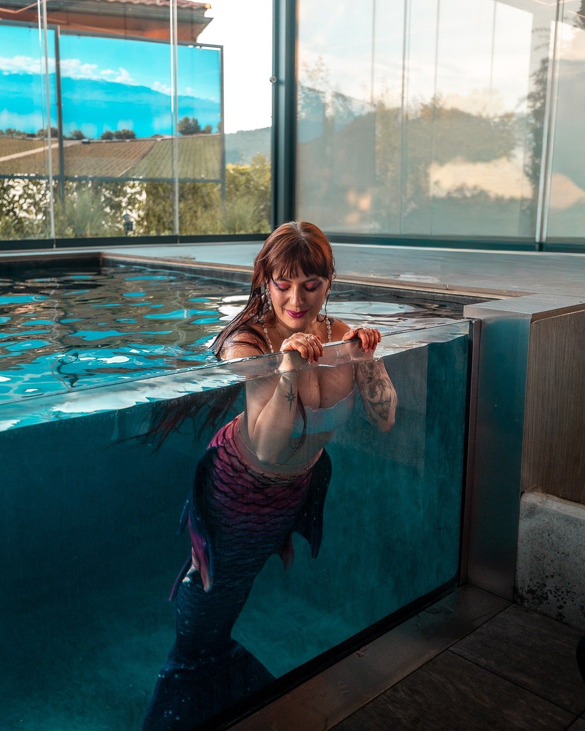 Une sirène accoudée à la paroi vitrée du bassin de Secret Paradise, la nageoire visible sous l'eau